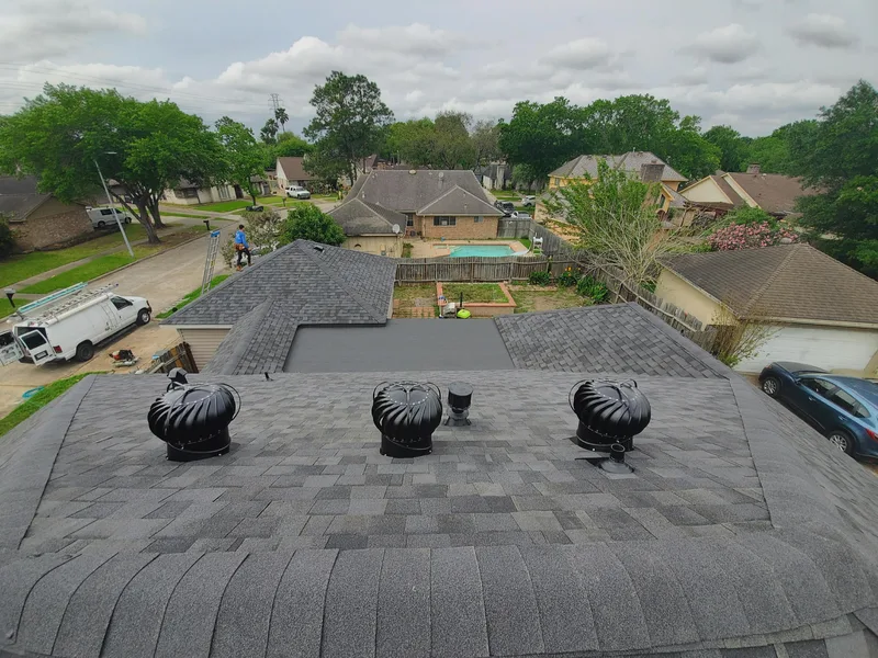 Aerial view across a grey shingle roof with three turbine vents, over a suburban street.