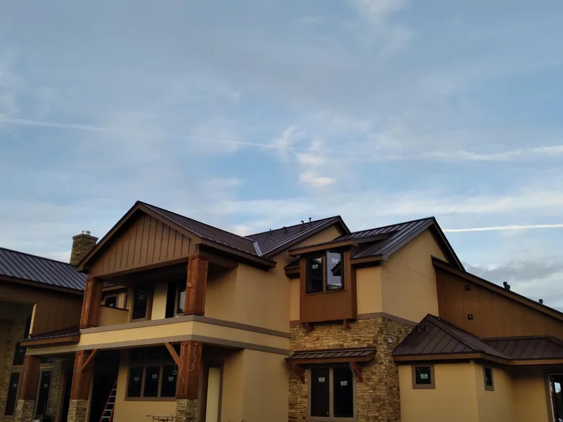 Dark standing-seam metal roof on a large stucco and stone home.