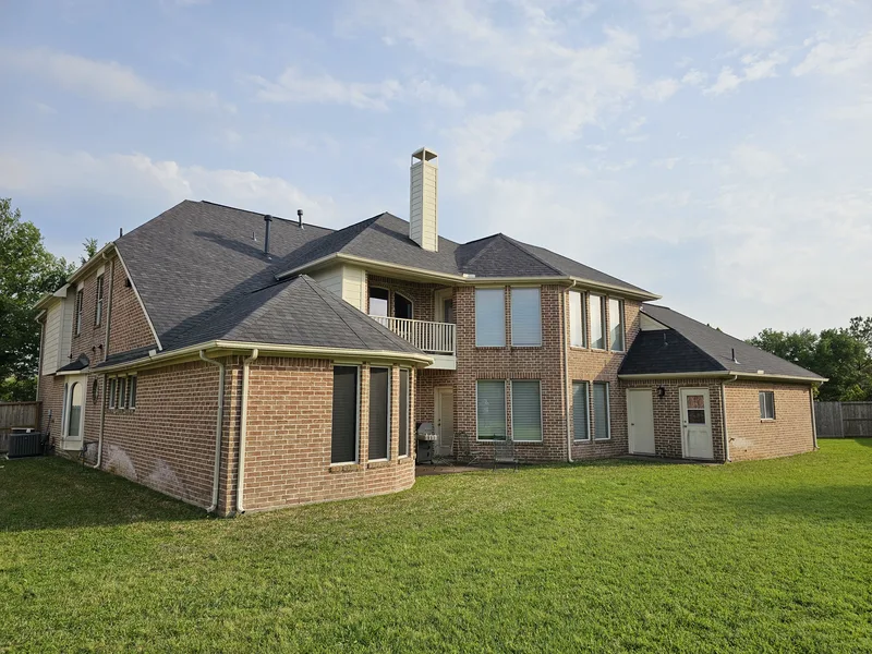 Rear elevation of a two-storey brick home with a dark shingle roof and a tall chimney.
