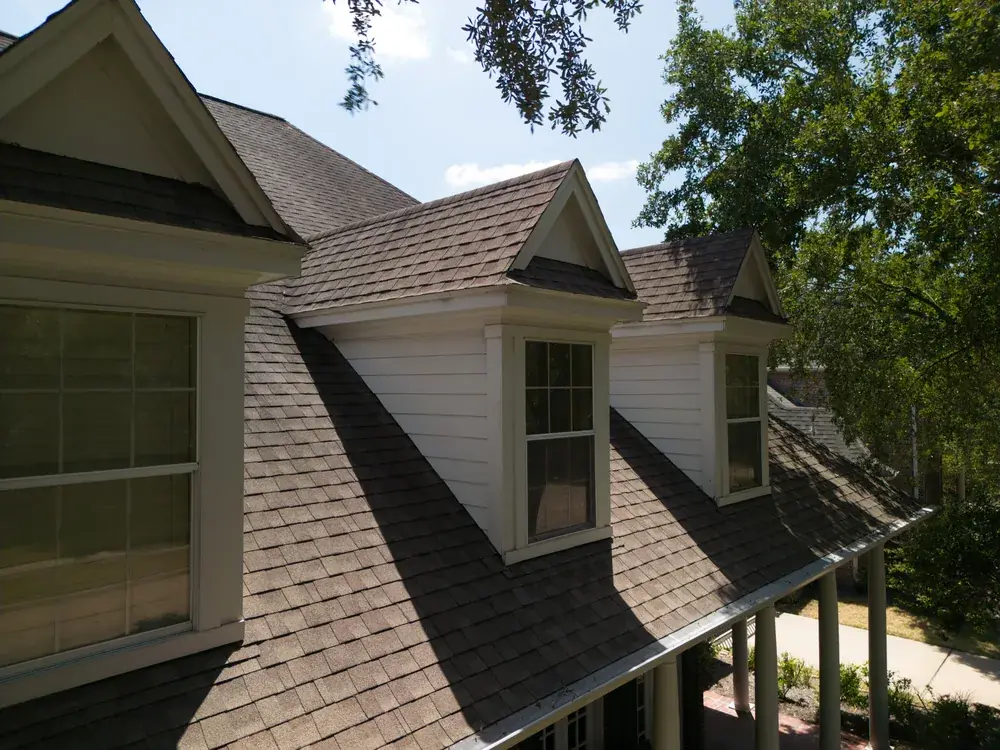 Close-up of newly installed architectural asphalt shingles and dormer windows on a two-story home.