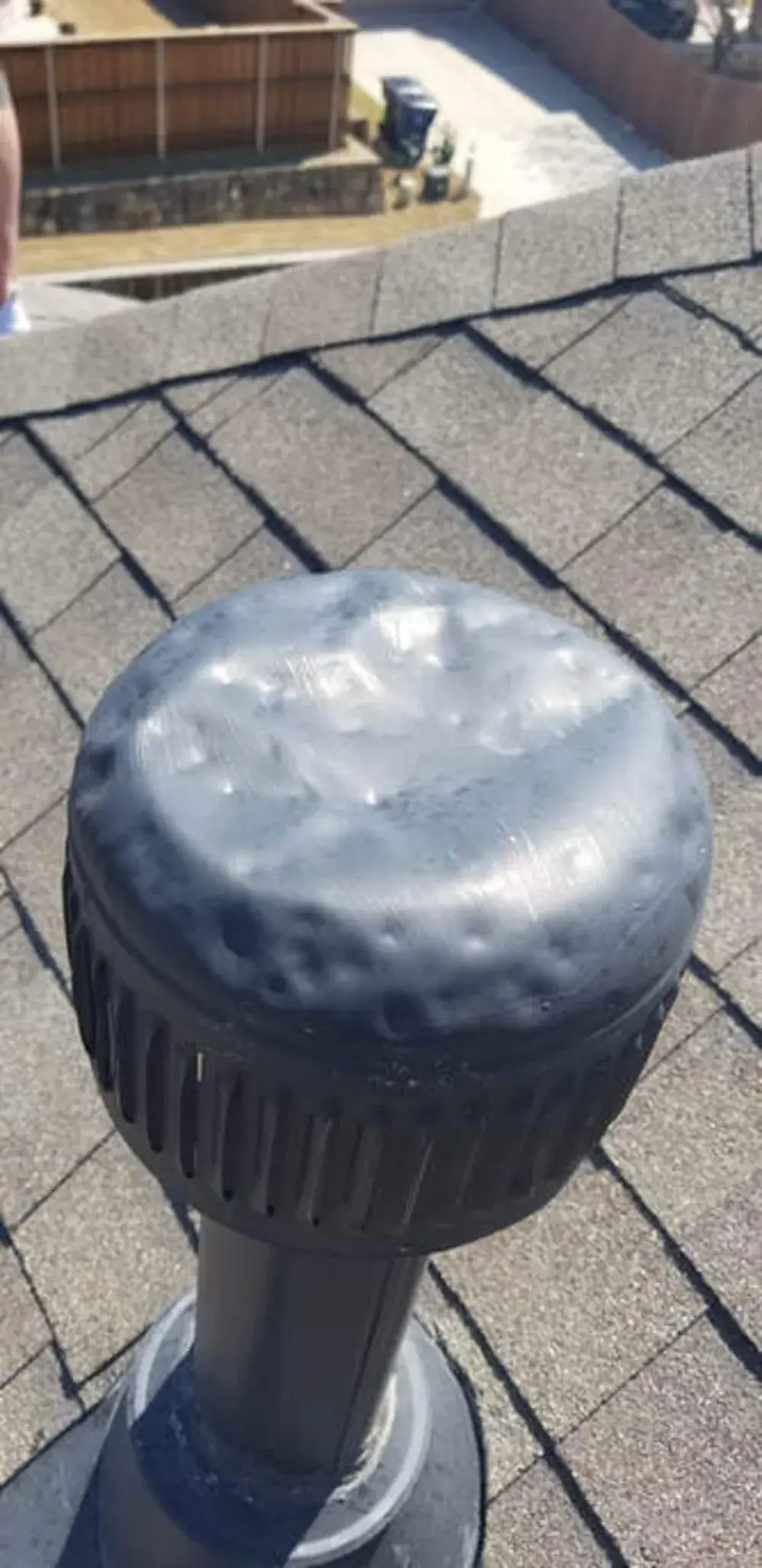 Hail dents across the metal cap of a roof turbine vent on a shingle roof.